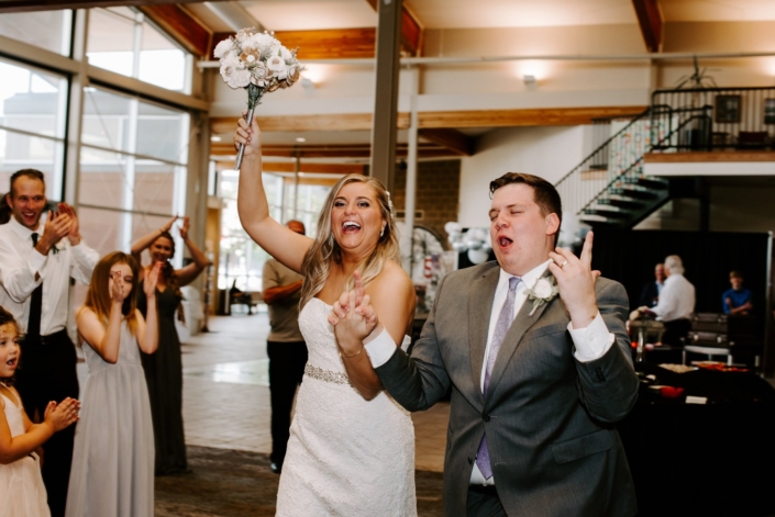 Bride and groom entering their reception with guests cheering.