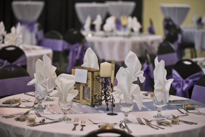 Wedding table setup with purple accents and folded white napkins.