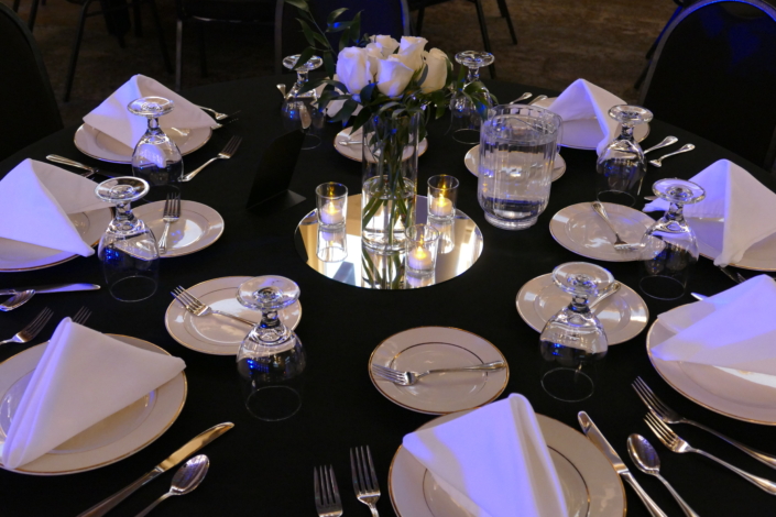 Elegant black linen wedding table setup with white roses and candles.