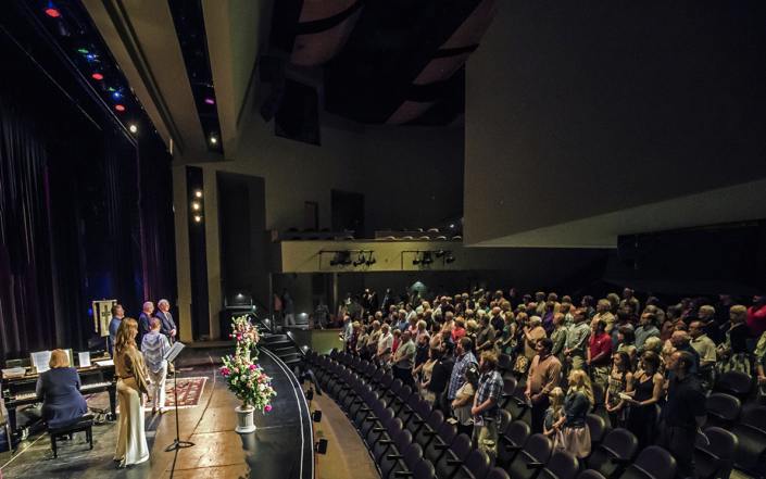 Wedding ceremony taking place on the theater stage with guests standing.