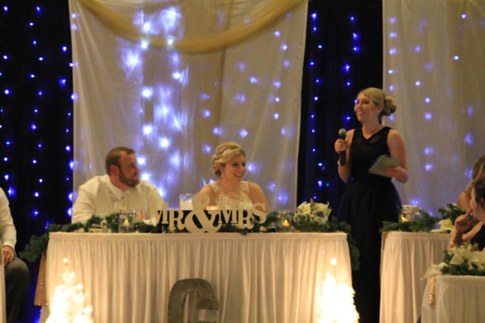 Head table with bridal party as a bridesmaid gives a toast.