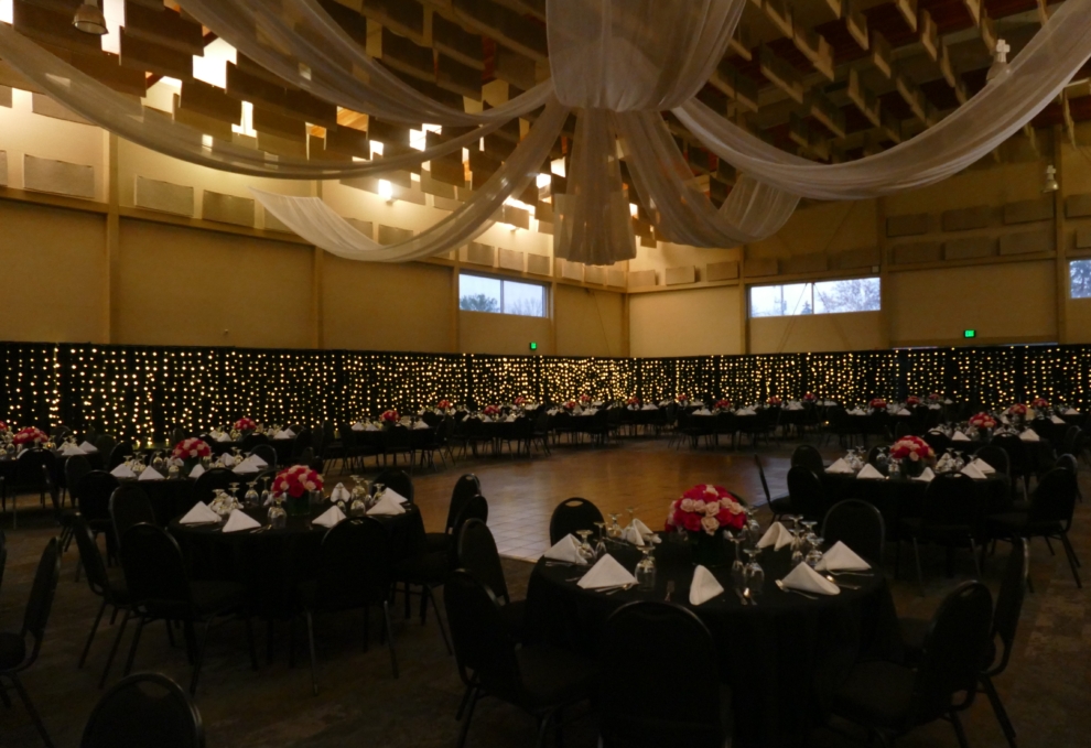 Wide view of the Expo Hall decorated for a wedding reception with black linens, twinkle lights, and draped ceilings at the Fairfield Arts & Convention Center in Fairfield, Iowa.