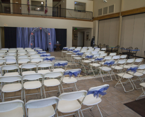 Indoor wedding ceremony setup in the Atrium at the Fairfield Arts & Convention Center in Fairfield, Iowa, with rows of white chairs and blue ribbon décor.