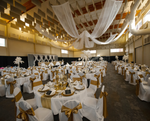 Wedding reception setup in the Expo Hall at the Fairfield Arts & Convention Center in Fairfield, Iowa, featuring elegant gold and white décor and ceiling draping.