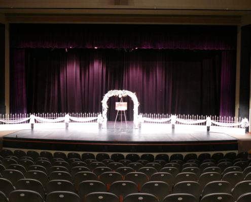 Wedding ceremony setup on the stage of the Theater at the Fairfield Arts & Convention Center in Fairfield, Iowa, with arch décor and auditorium seating.